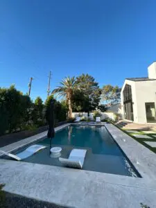 A pool with an umbrella and chairs in the middle of it.