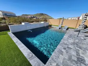 A pool with a stone wall and grass in the back.